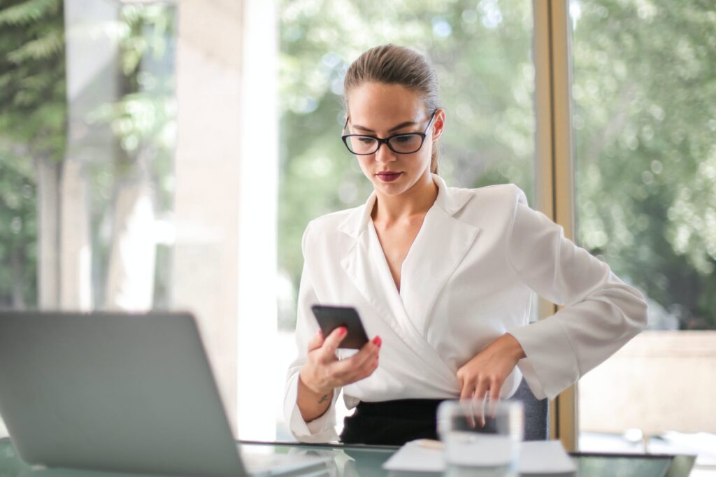 woman in white blazer holding black smartphone