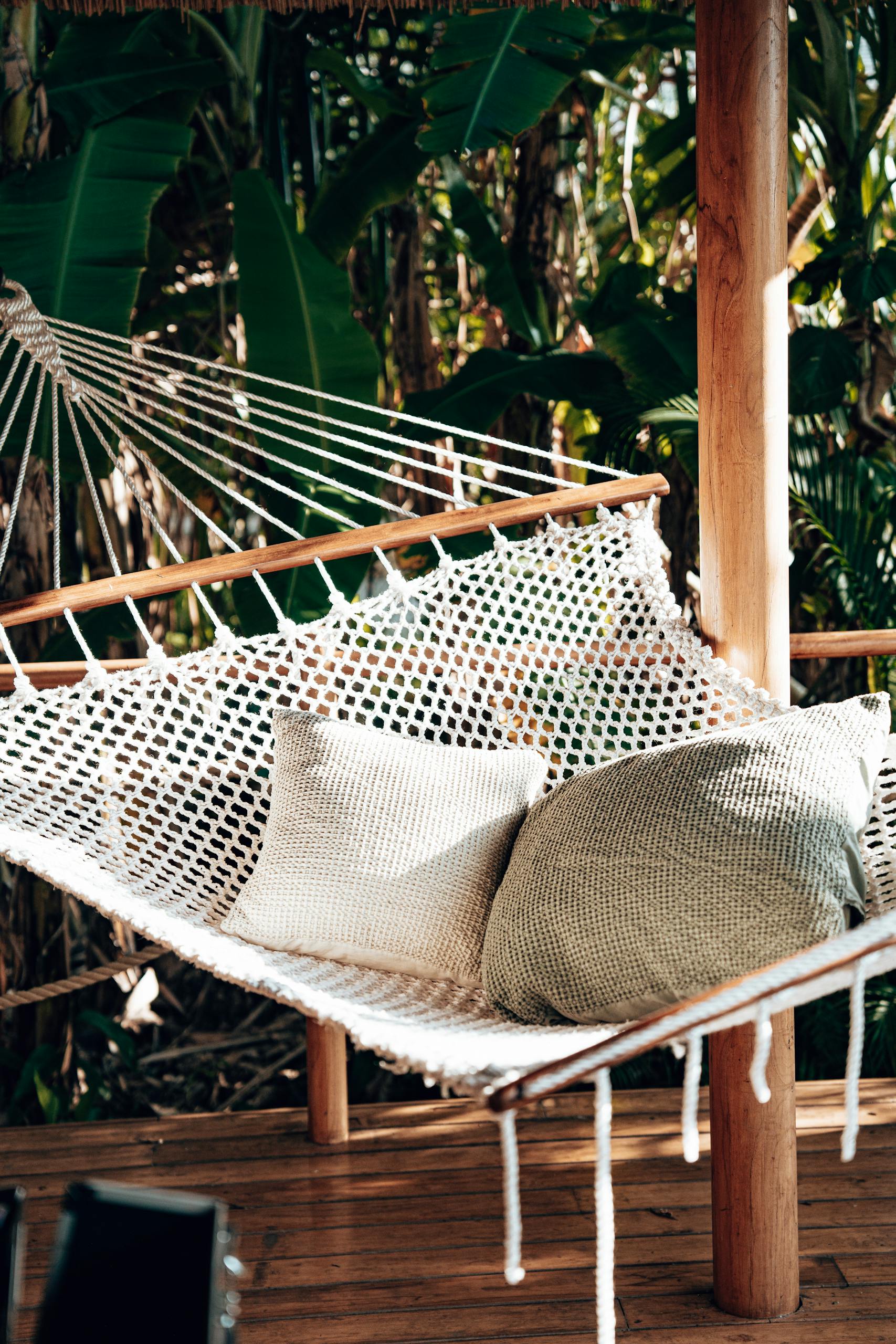 A cozy hammock with pillows in a tropical setting on a wooden verandah surrounded by lush greenery in Tanzania.