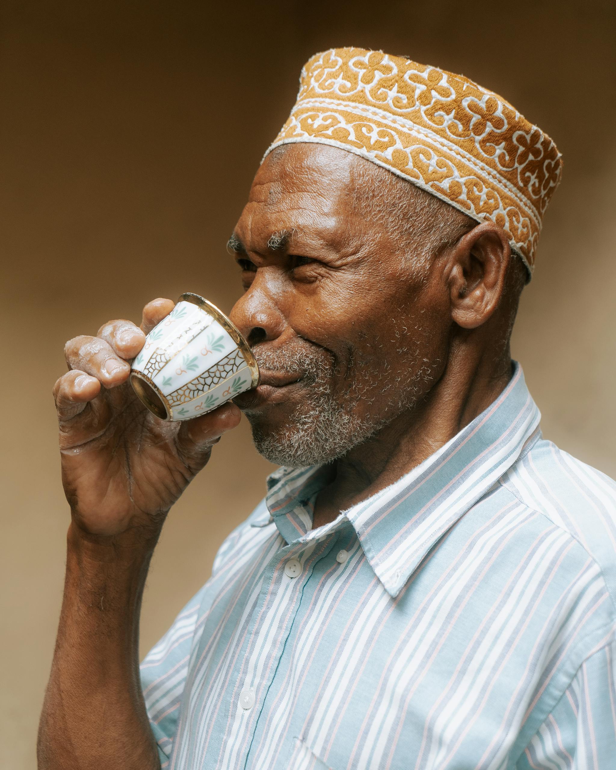 An elderly man savoring tea in traditional attire in Zanzibar, Tanzania.