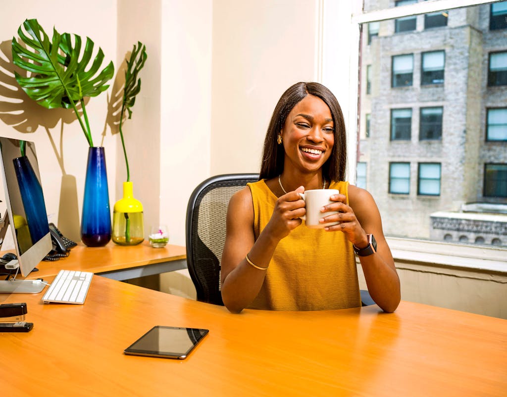 Confident woman in office attire enjoying a coffee break, showcasing modern workspace vibes.