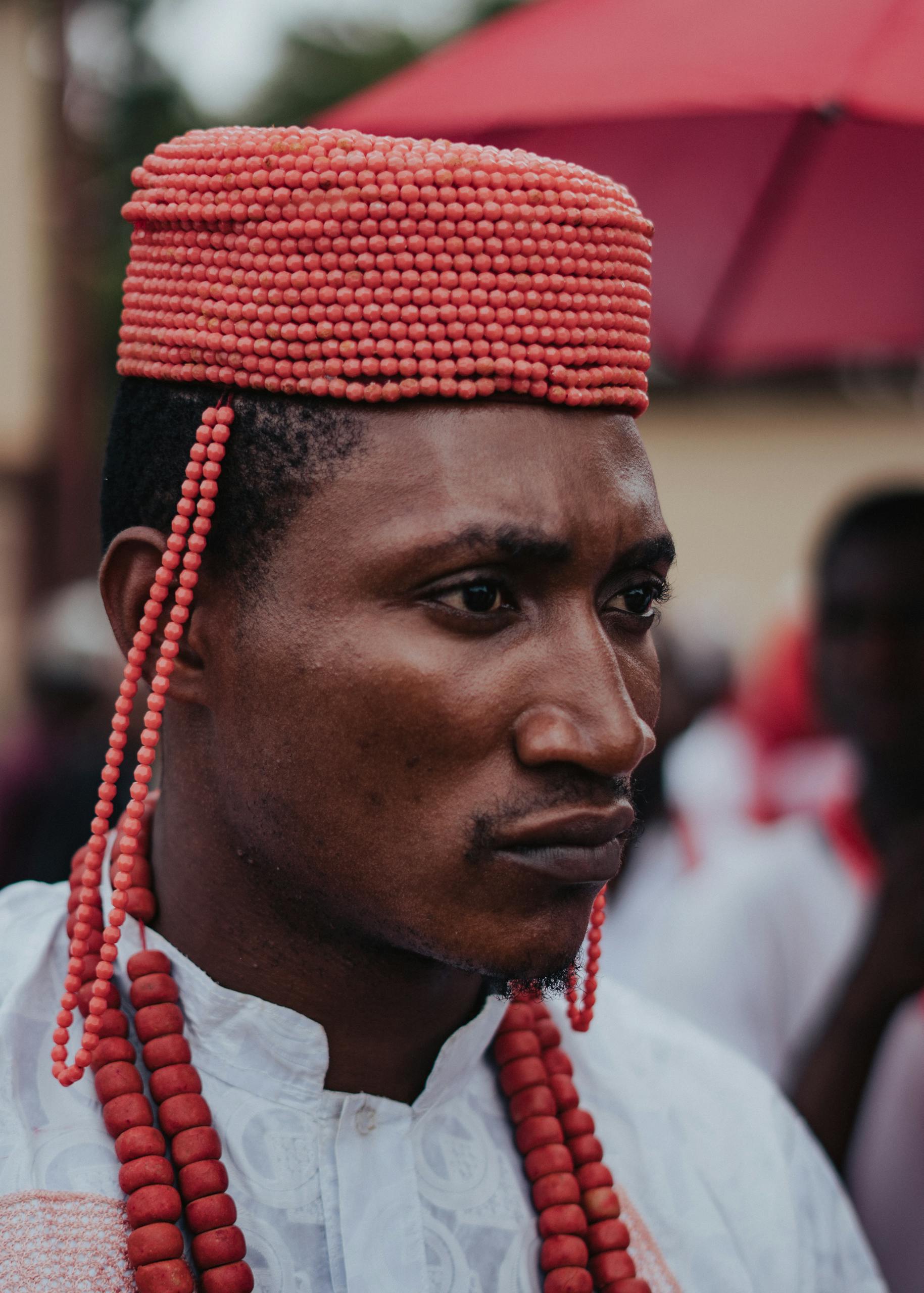 Portrait of a man in traditional Nigerian attire with a beaded cap and necklace, outdoors.