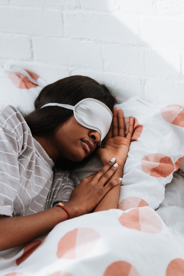 A woman wearing a sleep mask rests peacefully in a striped shirt, surrounded by patterned bedding.