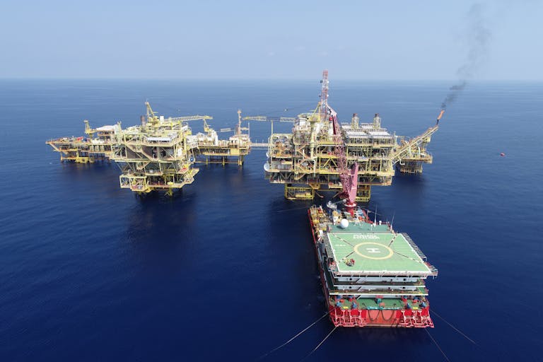 Aerial shot of multiple offshore oil platforms in a serene, blue sea under clear skies.