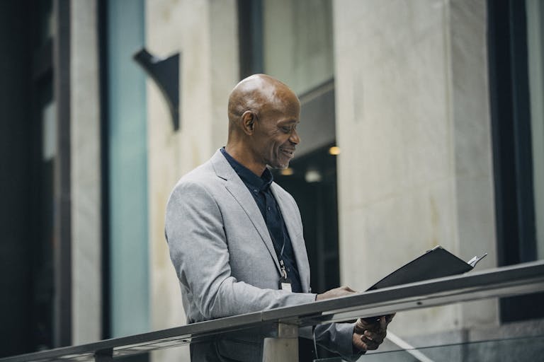 Middle-aged man in formal attire reviewing documents outdoors, exuding confidence and professionalism.