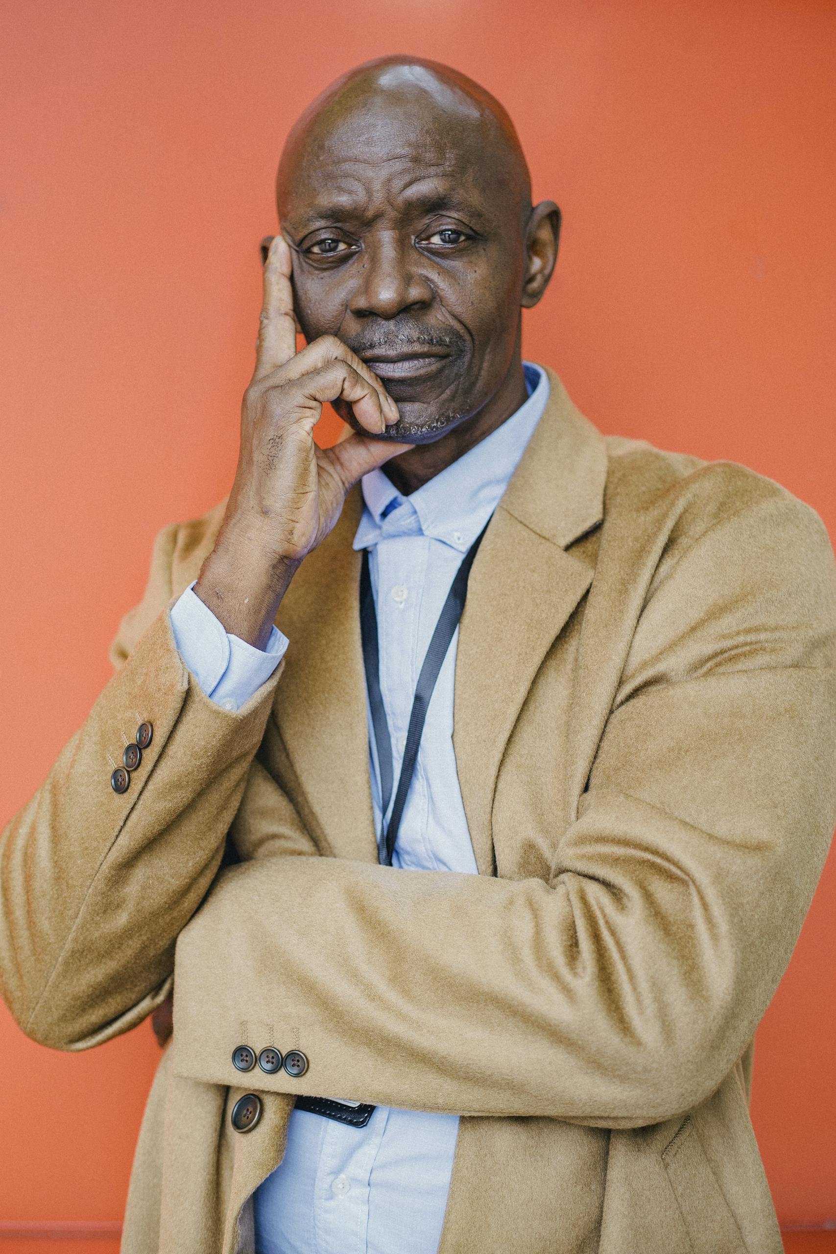 Portrait of a confident, mature man in a stylish camel coat against a vivid orange background.