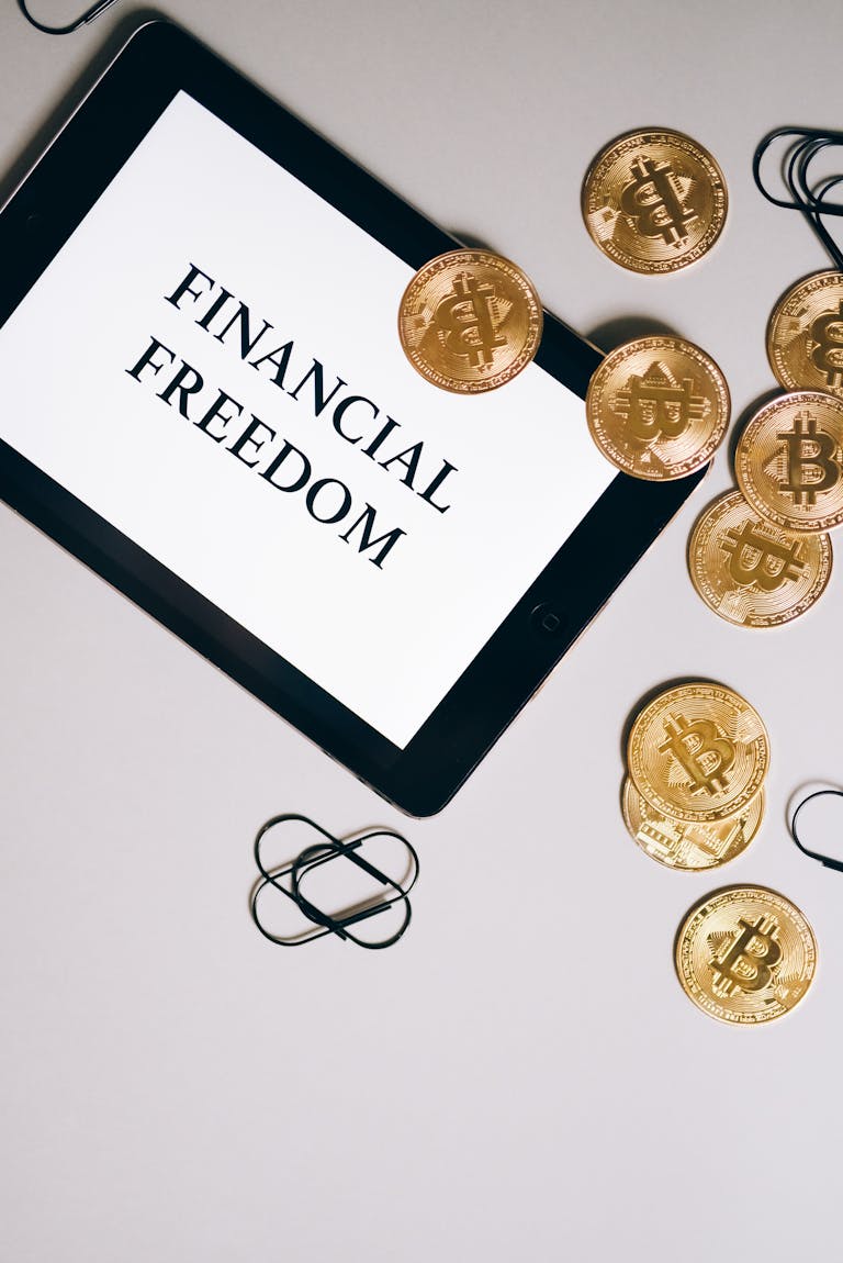 Top view of a tablet displaying 'Financial Freedom' with Bitcoin coins scattered around.