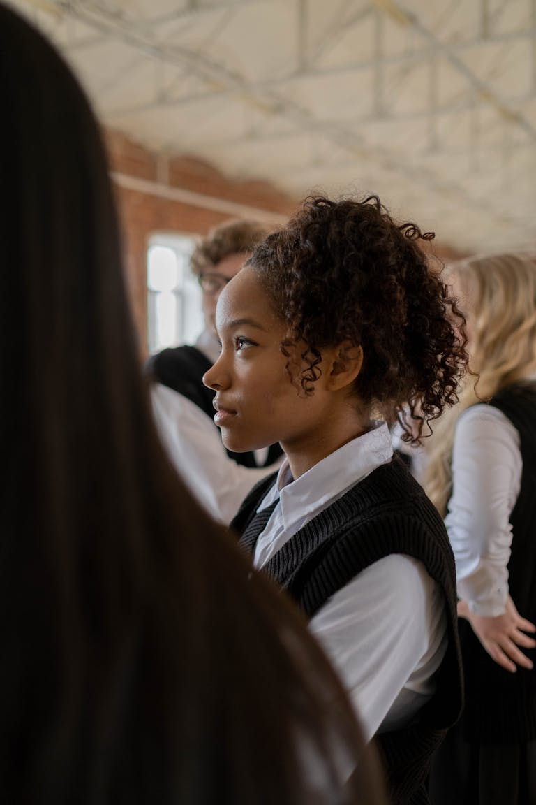Profile of a teenage girl with curly hair in a school uniform, indoors.