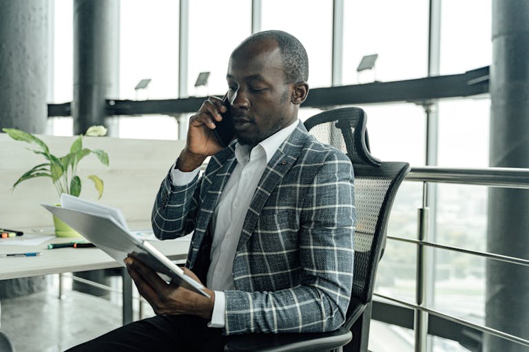 Professional businessman discussing documents during a phone call in a modern office setting.