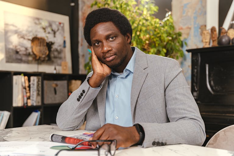Professional man in a gray suit sitting at a desk in a modern office, appearing thoughtful.