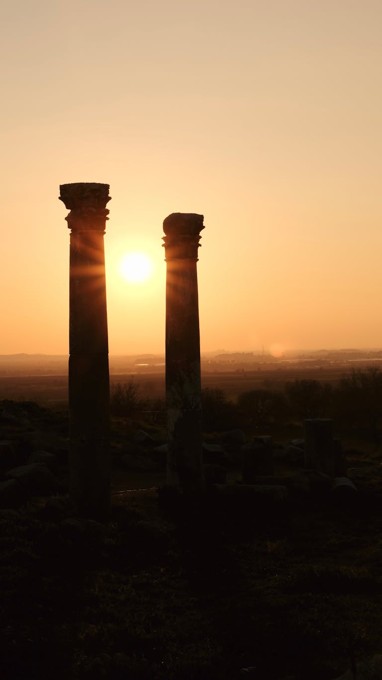 Silhouetted ancient columns against a stunning sunset sky in a rural landscape.