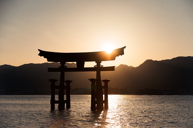 The iconic Itsukushima Shrine Torii Gate silhouetted against a stunning sunrise in Hiroshima, Japan.