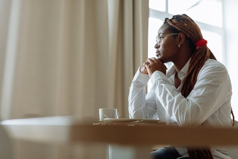 Side view of a pensive person with dreadlocks in a white shirt, enjoying coffee indoors.