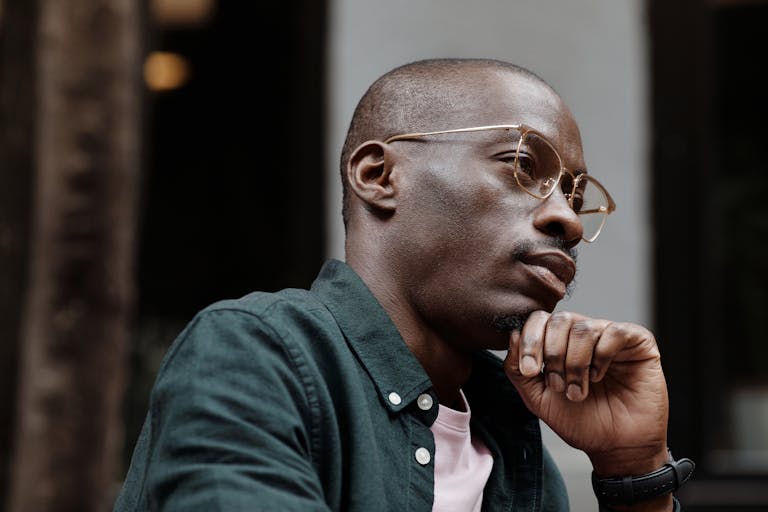 Thoughtful man with glasses sitting outdoors in contemplation.